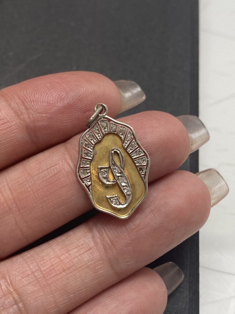 Colgante antiguo de oro 8K y diamantes con un emblema central en relieve, rodeado por un marco con detalles grabados. La pieza muestra un refinado trabajo artesanal típico del estilo Art Deco.