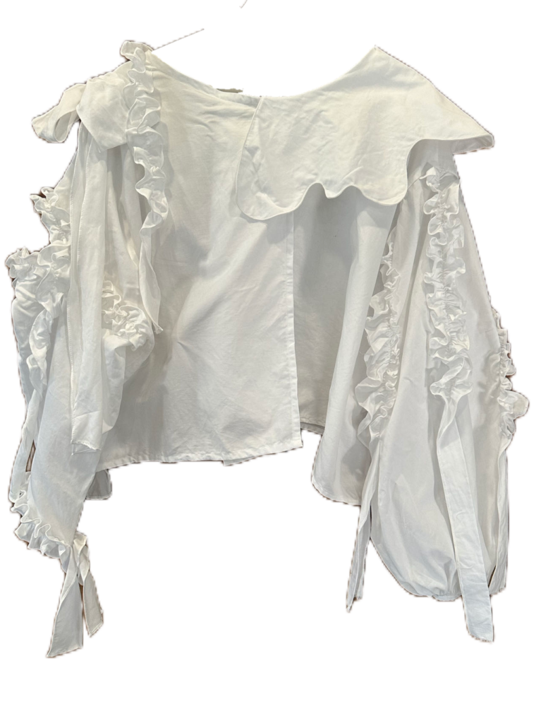 Blusa blanca de diseño asimétrico con volantes decorativos, manga abullonada y detalles románticos.